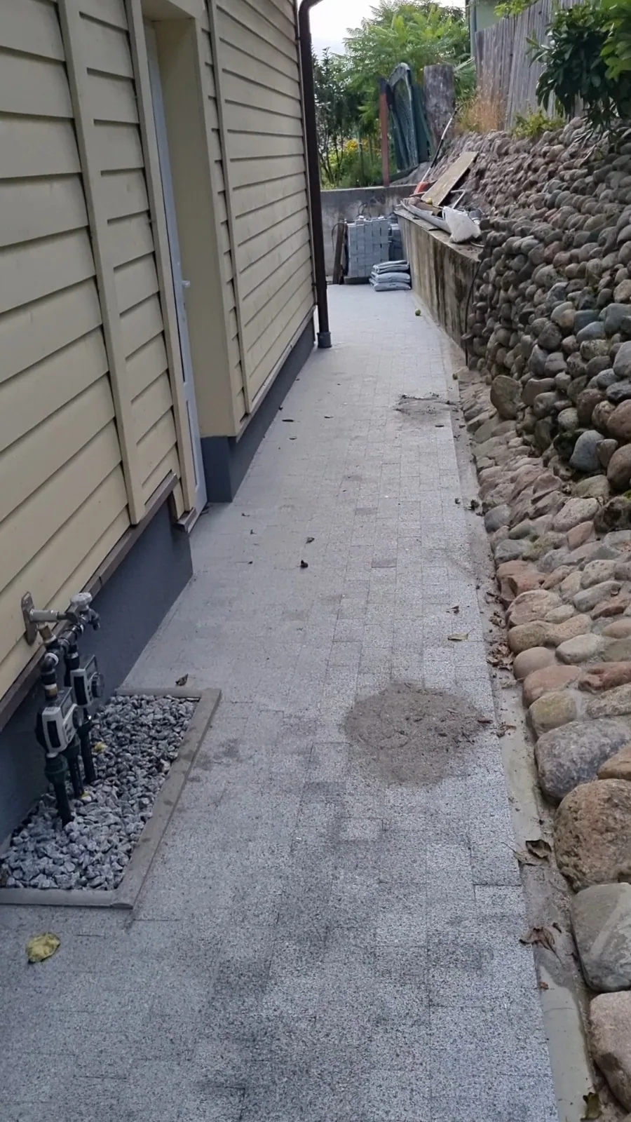 Baigtas siauras takas tarp namo ir akmenų šlaito, kadras iš vaizdo įrašo